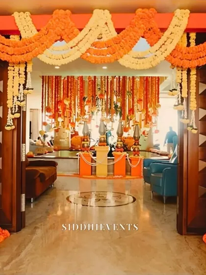 A stunning entrance for a Haldi or wedding ceremony, framed with bright orange marigold garlands and leading into a room filled with hanging floral decorations.