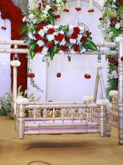 A close-up of a traditional silver-coated cradle, decorated with rich red and white flowers. This classic combination is perfect for a ceremony that feels both regal and pure.