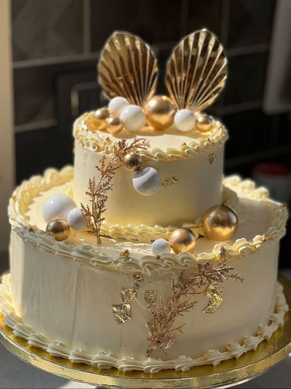A luxurious two-tiered wedding cake in white and gold. This design features gold leaf, decorative spheres, and intricate gold toppers for a truly show-stopping effect.