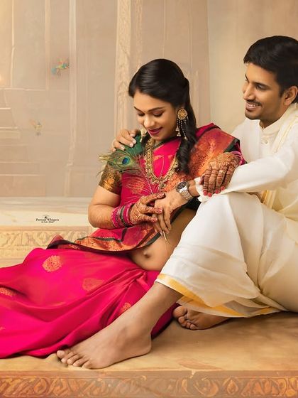 A playful and romantic moment between a couple. Seated on the steps of the painted backdrop, the husband gently touches his wife's face with a peacock feather.