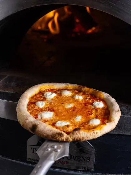 A classic cheese pizza going into the wood-fired oven, where it will transform into a bubbly, charred masterpiece.