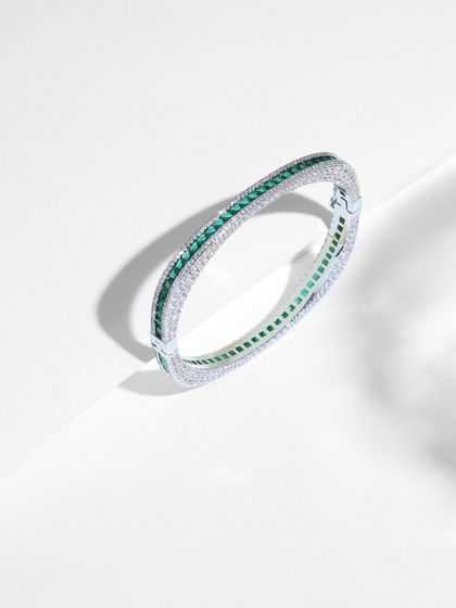 This 14k gold bangle showcases a modern, geometric design. It features a line of princess-cut emeralds bordered by round-cut diamonds, perfect for those who love quiet luxury.
