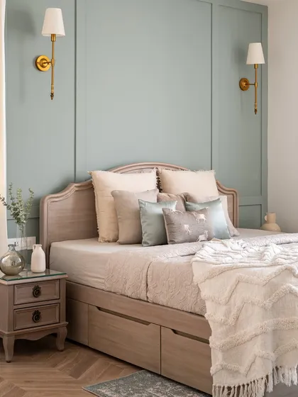 A bedroom in our Riviera Maison project, featuring a soft sage-green paneled wall and a custom bed with built-in storage drawers. The brass wall sconces add a touch of classic elegance.