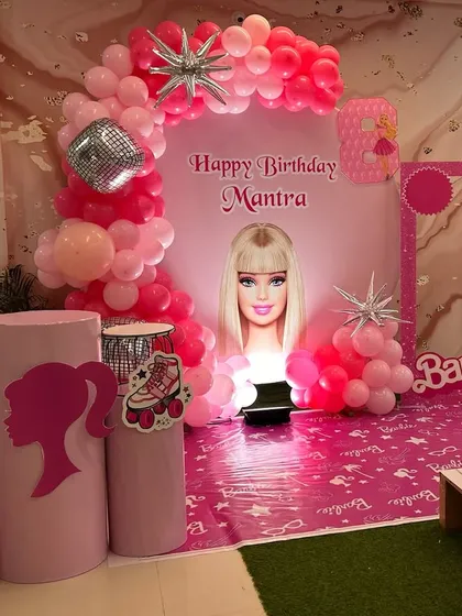 An all-pink Barbie themed birthday setup. This decoration features a Barbie-head silhouette on the backdrop, themed props like lipstick and roller skates, and various shades of pink balloons.
