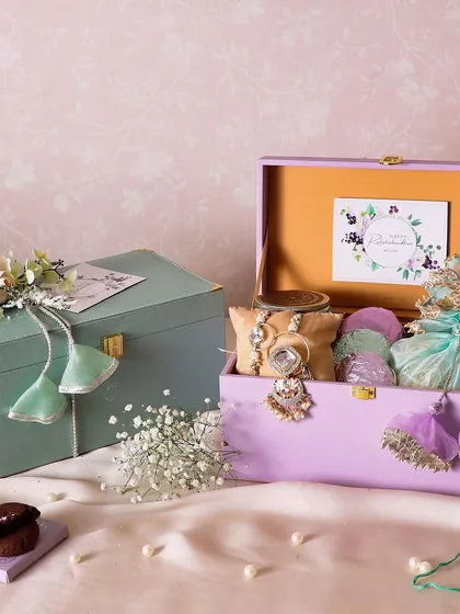 The Jade Joy Hamper is a beautiful gift option, available in two colors. It contains a jar of brownie bites, a potli of peanuts, fudge cookies, and a Rakhi set.