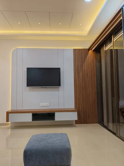 A minimalist TV unit design featuring a clean white panel against a wood-textured wall. The floating console keeps the floor clear, making the room feel more spacious and modern.