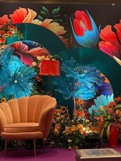 A seating area from the Bhaat ceremony, with a stylish scalloped armchair set against the bold, floral backdrop. The decor is a playful and modern take on traditional celebration design, using color and pattern to create a joyful atmosphere.