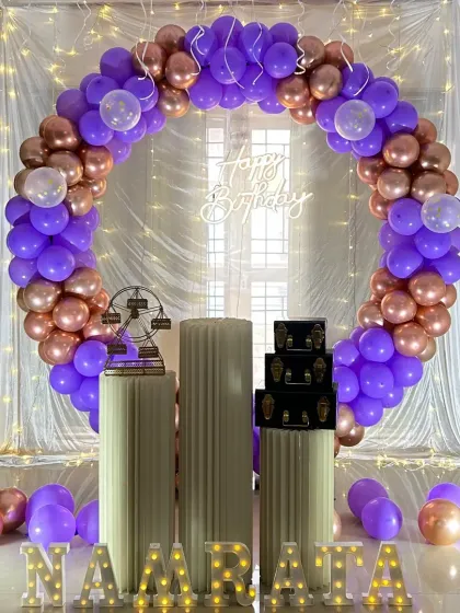 A grand circular balloon arch in purple and rose gold. This setup is perfect for a milestone birthday, with a fairy light curtain backdrop and marquee letters for a personalized touch.