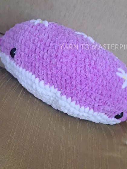 A side view of the purple whale pillow, showing its plump shape and cute little fins. It's perfect for cuddling or as a decorative pillow.