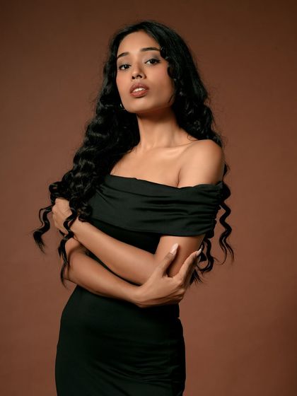 A classic and elegant studio portrait. The off-shoulder black dress and the model's confident gaze create a timeless look, perfect for a sophisticated fashion brand.