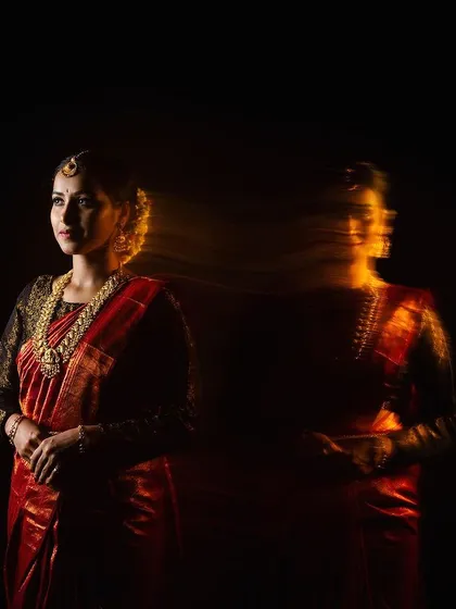 An experimental portrait using the shutter drag technique to create a ghostly motion effect. This image of a model in a traditional red saree against a black background highlights our artistic approach and technical skill in creative studio photography.