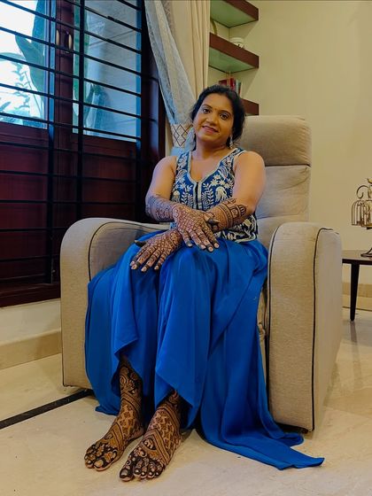 A happy client relaxing after her full bridal mehendi session, covering both hands and feet.