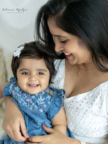A close-up of a mother and her smiling baby girl. The baby's happy face looking right at the camera makes this an incredibly engaging and heartwarming portrait.