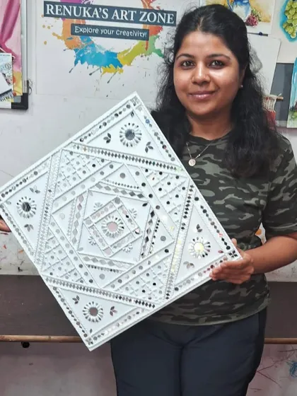The proud smile of a student holding her completed Lippan art piece. In our classes, you will learn to create these beautiful, traditional mud and mirror designs to decorate your home.