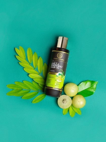 A simple, elegant shot of a hair oil with its key ingredient, amla. The clean teal background provides a beautiful contrast.
