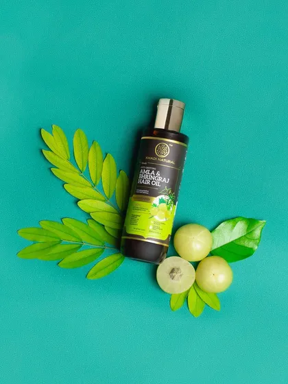 A top-down flat lay of a hair oil with its main ingredients, amla. The vibrant teal background makes the green elements pop, creating a fresh and natural composition.