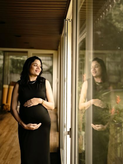A beautiful indoor portrait using reflections. The mom-to-be stands by a window, her reflection captured in the glass, adding a layer of depth and introspection to the shot.