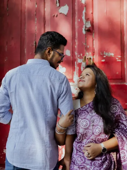 A lovely shot of the couple against a rustic red door, creating a vibrant and textured background for their pre-wedding portrait.