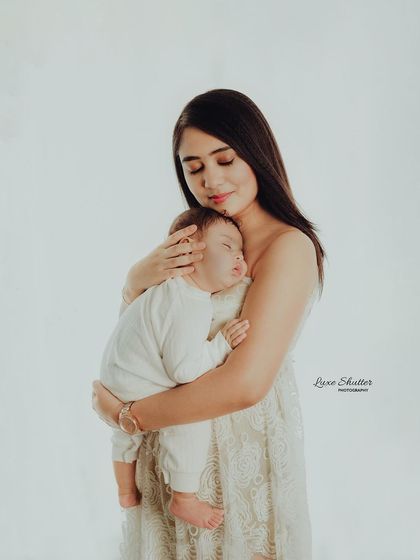 A mother holds her sleeping baby close. The simplicity of the white outfits and bright lighting creates a pure and timeless portrait.
