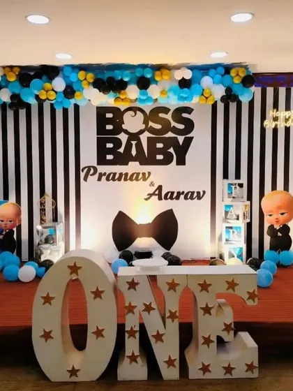 A stylish Boss Baby theme for a first birthday celebration. The stage features a black and white striped backdrop, character cutouts, and large 'ONE' marquee letters.
