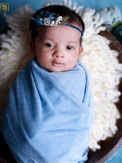 A full shot of the awake baby in the blue wrap, looking right at the camera.