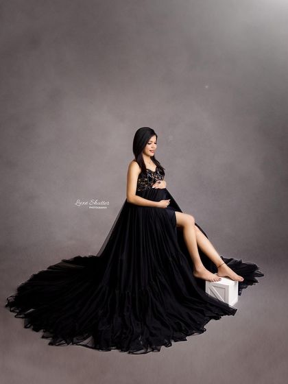 A glamorous seated portrait in a black tulle gown. The simple grey backdrop and classic pose create a look of timeless sophistication.