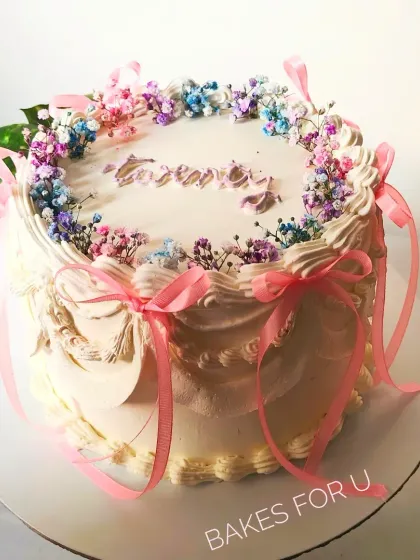 A gorgeous vintage-style cake decorated with delicate piping, pink ribbons, and a crown of colorful dried baby's breath.