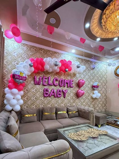 A beautiful welcome for a little princess at her Nani's home. This setup features a lovely balloon half-arch in shades of pink and white over the sofa, creating an elegant and warm photo spot.