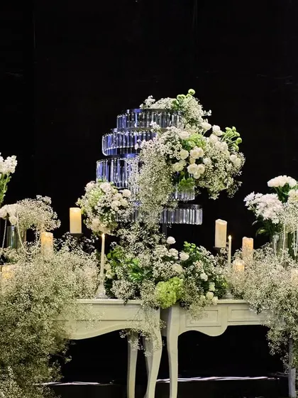 A console table decorated with a cascade of baby's breath and white florals, with a tiered crystal centerpiece. The dark background makes the white elements pop.