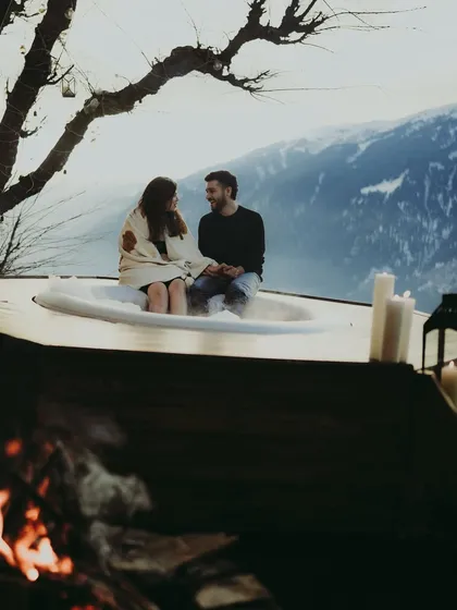 A proposal can be an entire experience. Here, a couple shares a quiet moment in a mountain-view hot tub, complete with a cozy fire, as part of their planned proposal getaway in the Himalayas.