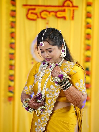 This bride is adjusting her floral jewelry. The hairstyle is designed to hold these delicate accessories securely throughout the Haldi ceremony.