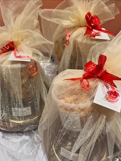 A collection of gift hampers elegantly wrapped in sheer fabric with a bright red ribbon. These custom arrangements can hold jars of cookies, nuts, or small cakes.