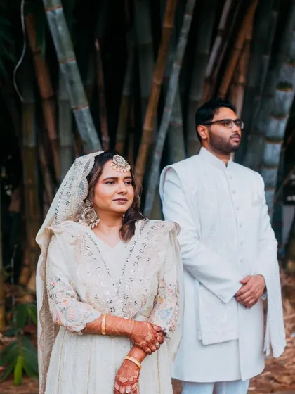 A serene portrait of a couple on their wedding day, dressed in elegant white attire for their Muslim wedding ceremony, captured against a natural bamboo backdrop.