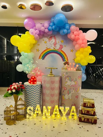A sweet unicorn themed birthday party. The setup features a circular backdrop with a unicorn and rainbow, a pastel balloon arch, and a personalized name sign in light-up letters.