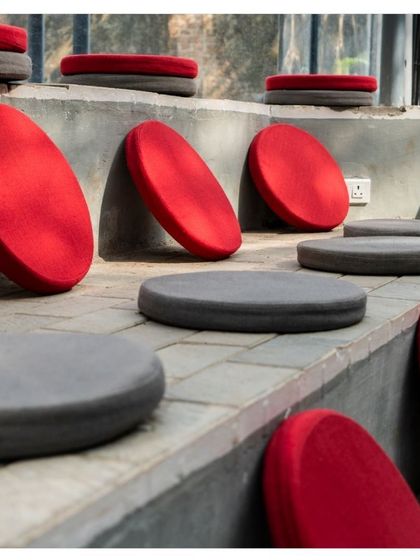 The tiered seating inside the Koodaaram pavilion, made of simple concrete steps with colorful cushions. The open roof structure allows for natural ventilation and a connection to the sky.