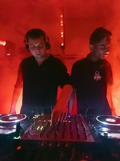 A close-up of two DJs collaborating on the decks during a high-energy set. The red lighting and focused expressions capture the intensity and artistry that define our music events.