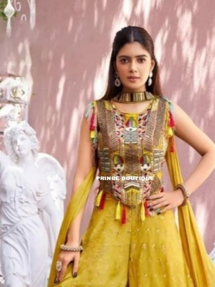 A stylish mustard yellow Indowestern outfit featuring wide-leg palazzo pants and a heavily embroidered top with colorful tassels. It's a fun and fashionable choice for a haldi or sangeet.