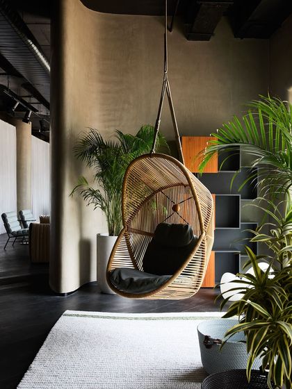 A hanging wicker chair creates a relaxed, bohemian vibe in this outdoor or semi-outdoor vignette. The use of numerous plants enhances the feeling of being in a garden.