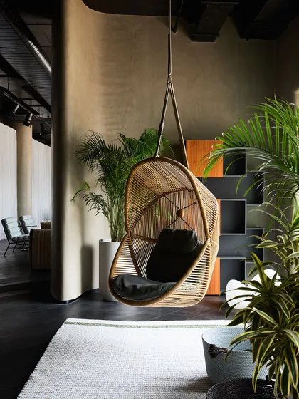 A hanging wicker chair creates a relaxed, bohemian vibe in this outdoor or semi-outdoor vignette. The use of numerous plants enhances the feeling of being in a garden.