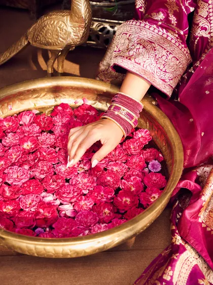 A detail shot focusing on the bride's hand, adorned with bangles, against a bowl of rose petals, capturing the essence of a traditional ceremony.