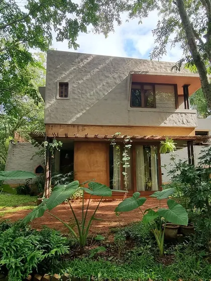 The exterior of the artist's residence is designed to blend into its wooded surroundings. The textured walls and large openings are softened by the lush foliage, making the house feel like a natural extension of the garden.