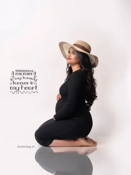 A stylish and modern solo portrait. The mom-to-be wears a simple black dress and a chic hat, looking up thoughtfully. This image has a contemporary and fashionable feel.