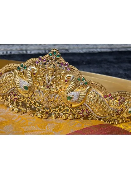 A statement Vaddanam, or waist belt, is what completes the bridal silhouette. This piece, with its twin peacock design and central goddess motif, is a work of art that beautifully accentuates the waist.