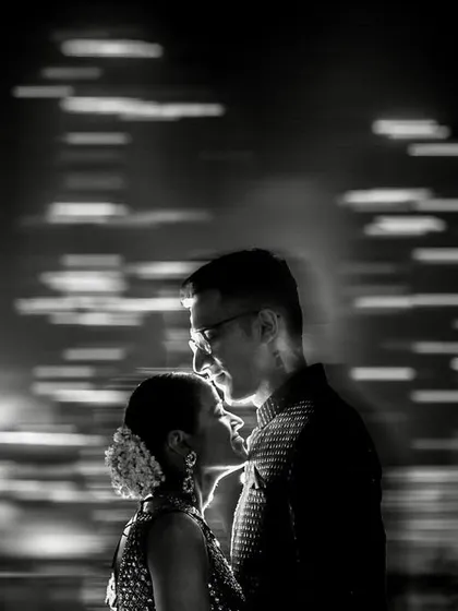 A creative black and white portrait using motion blur. The streaking lights of the cityscape in the background contrast with the calm, intimate moment shared by the couple.