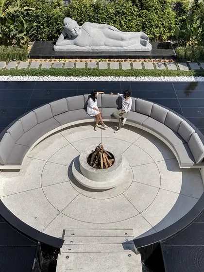 An aerial view of the sunken lounge shows its perfect circular geometry, creating an intimate gathering space within the larger landscape. It is a place for conversation and connection, set against a backdrop of serene greenery and water.