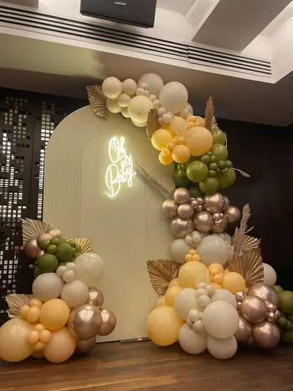 An elegant baby shower setup featuring an 'Oh Baby' neon sign and a beautiful organic balloon arch in earthy tones of olive green, peach, and metallic rose gold.