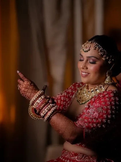A candid moment during the bridal getting-ready process, the bride smiles as she adjusts her bangles, the warm lighting creating an intimate feel.