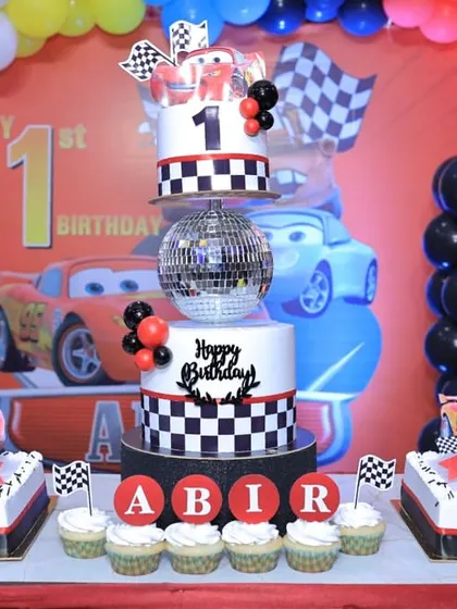 The complete dessert table for Abir's Cars-themed first birthday. It features a main tiered cake, two smaller flat cakes, and personalized cupcakes.