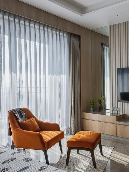 A cozy reading corner in a bedroom, featuring a comfortable orange armchair and ottoman. The neutral palette of soft grays and warm beiges creates a serene and tranquil haven.