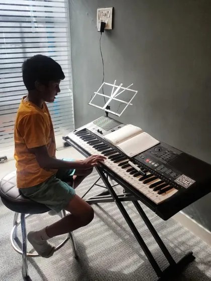 A young student diligently practices his keyboard lesson, reading from the sheet music in front of him.
